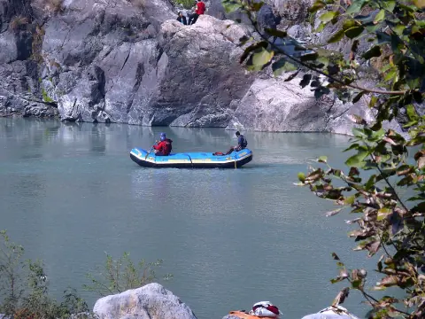 Blue raft with a guide and a guest on a calm stretch of the Ganga between rocky banks