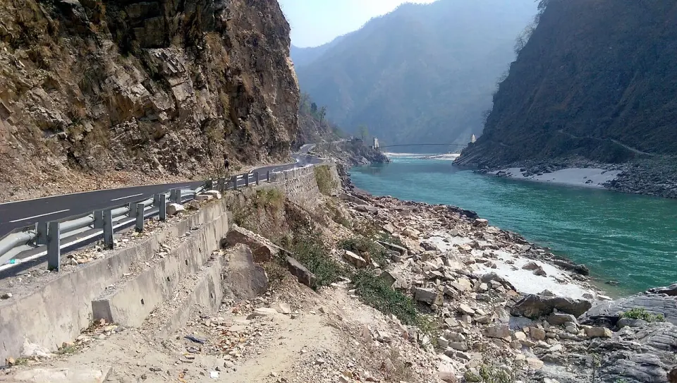 The Ganga running turquoise through a hill gorge beside a mountain road, with a suspension bridge in the distance