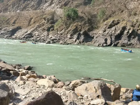 Rafts running a rapid on the green water of the Ganga below rocky hillsides near Rishikesh