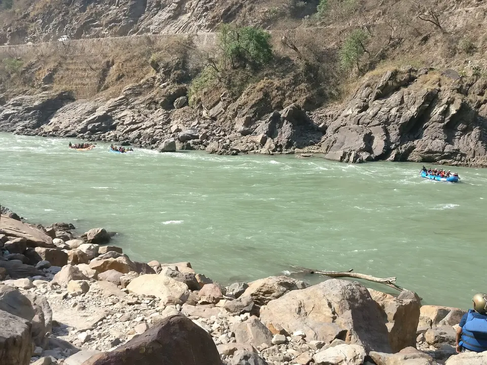 Rafts running a rapid on the green water of the Ganga below rocky hillsides near Rishikesh