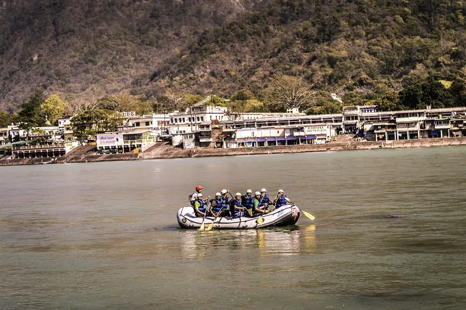 Raft of paddlers in helmets and life jackets on the Ganga in front of the ghats and buildings of Rishikesh