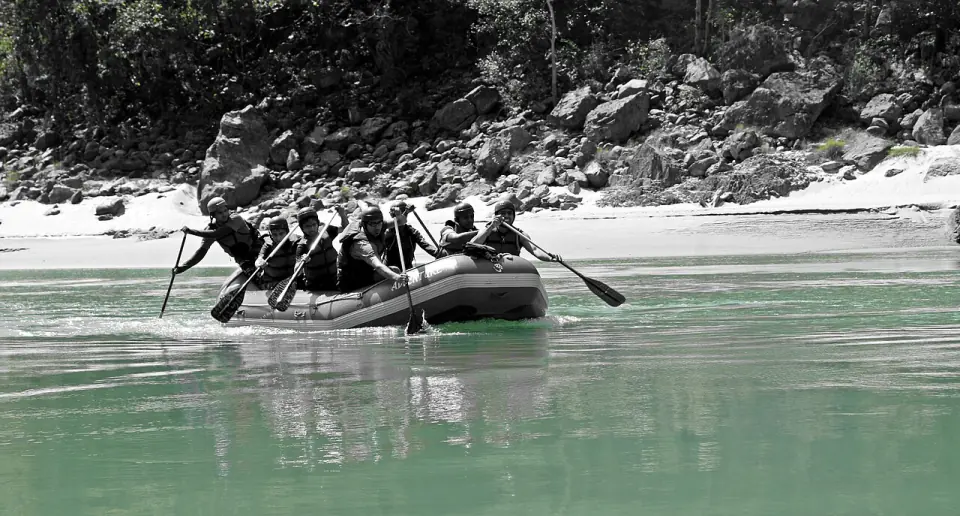 Rafters in helmets and life jackets paddling a grey raft across the green water of the Ganga
